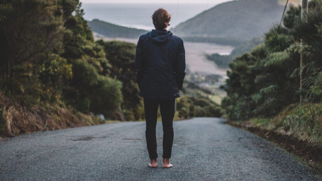 Bosá žena stojí na silnici a dívá se dolů z kopce. Každá terapie začíná prvním krokem. 